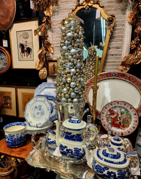 An ornate gold gilt mirror above a console styled with blue and white porcelain and a silver ornament tree