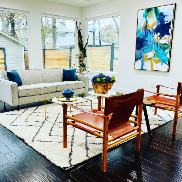 A staged living room with a linen sofa, leather sling chairs, a Moroccan rug and abstract art