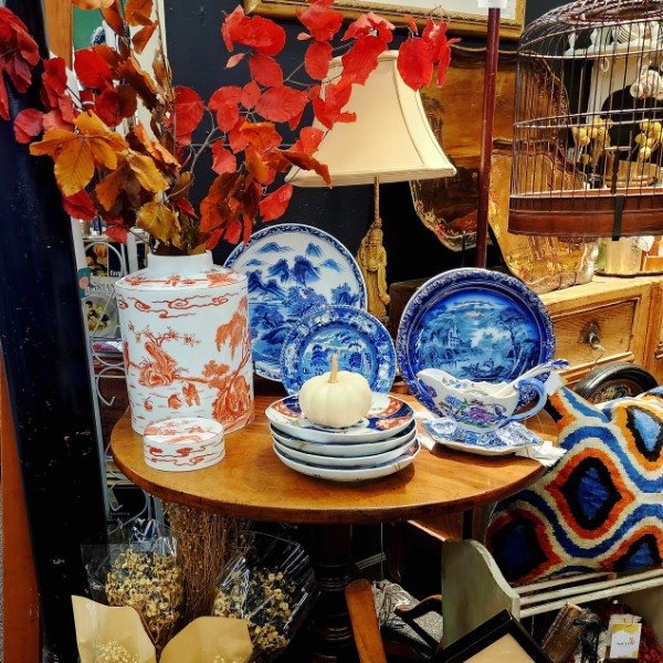 A round table styled with blue and white porcelain, an orange jar and autumn branches