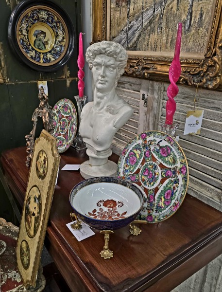 A plaster bust flanked by pink candles with famille rose plates and a porcelain bowl