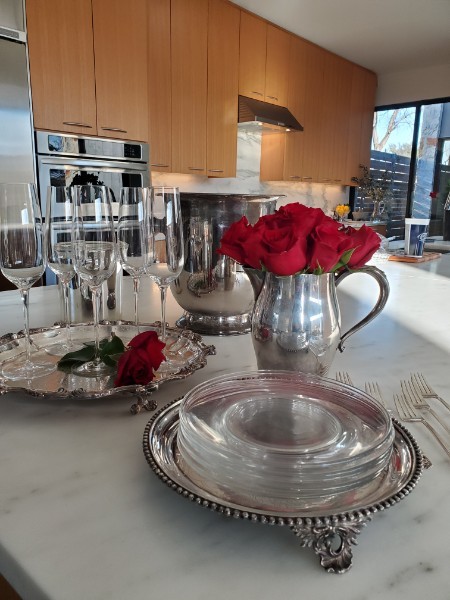 Antique silverplate trays, a pitcher of red roses and crystal glassware on a marble counter