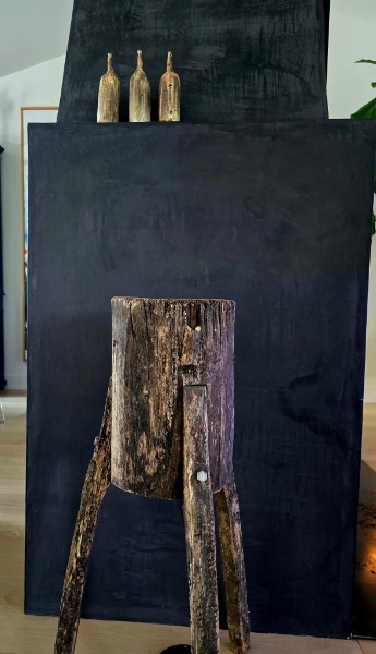 A primitive wood stump stool with three brass vessels against a blackened panel
