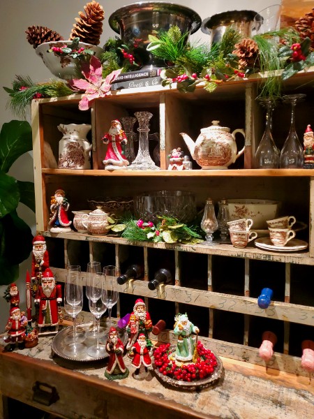 A rustic wine rack cabinet styled with vintage Santas, cut crystal and holiday greenery